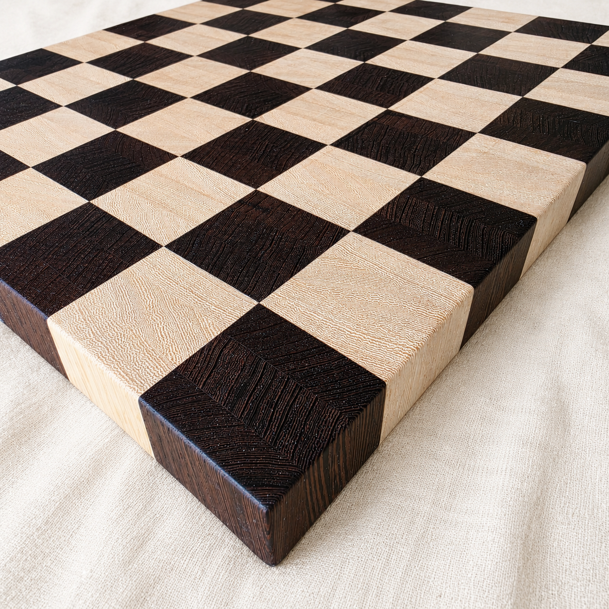 Angled view of the solid end-grain wenge and Lati chess board showing its 1 and 3/8 inch thickness and standing grain, on linen